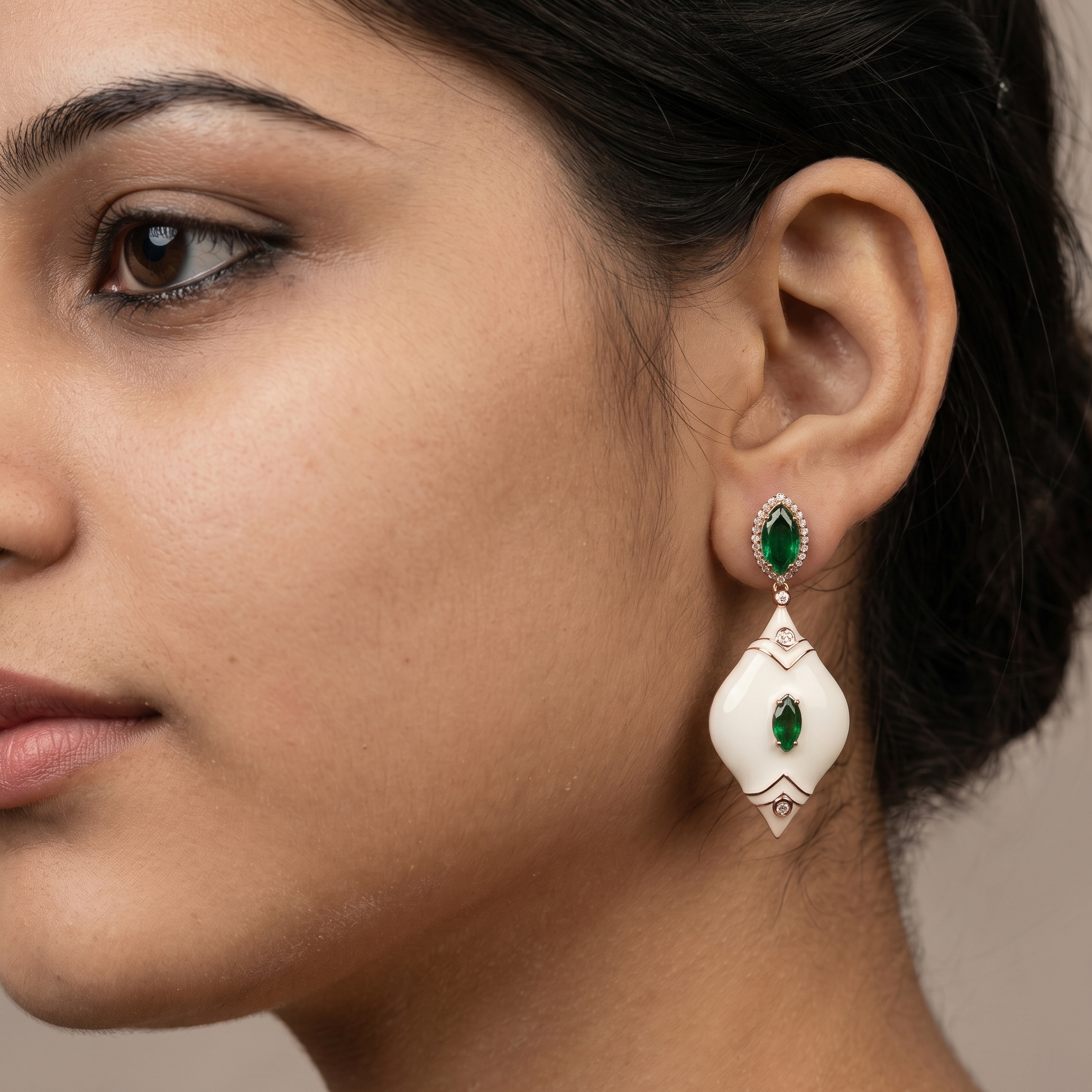 Close-up of a woman wearing a pair of earrings with green gemstones on a neutral background